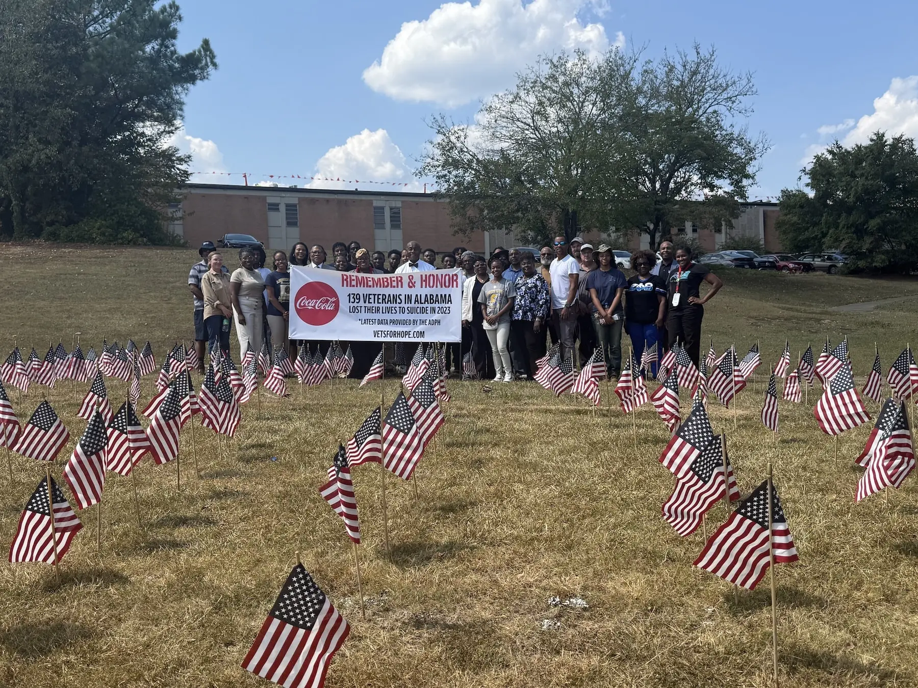 Group honoring Alabama veterans lost to suicide in 2023, with American flags displayed on a grassy field