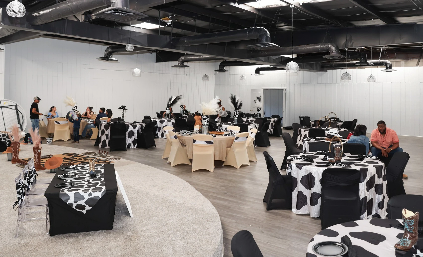 Event space with round tables set in black, white, and tan decor, featuring cow-patterned&nbsp;and cowboy-style&nbsp;tablecloths and centerpieces, with people seated throughout the room.